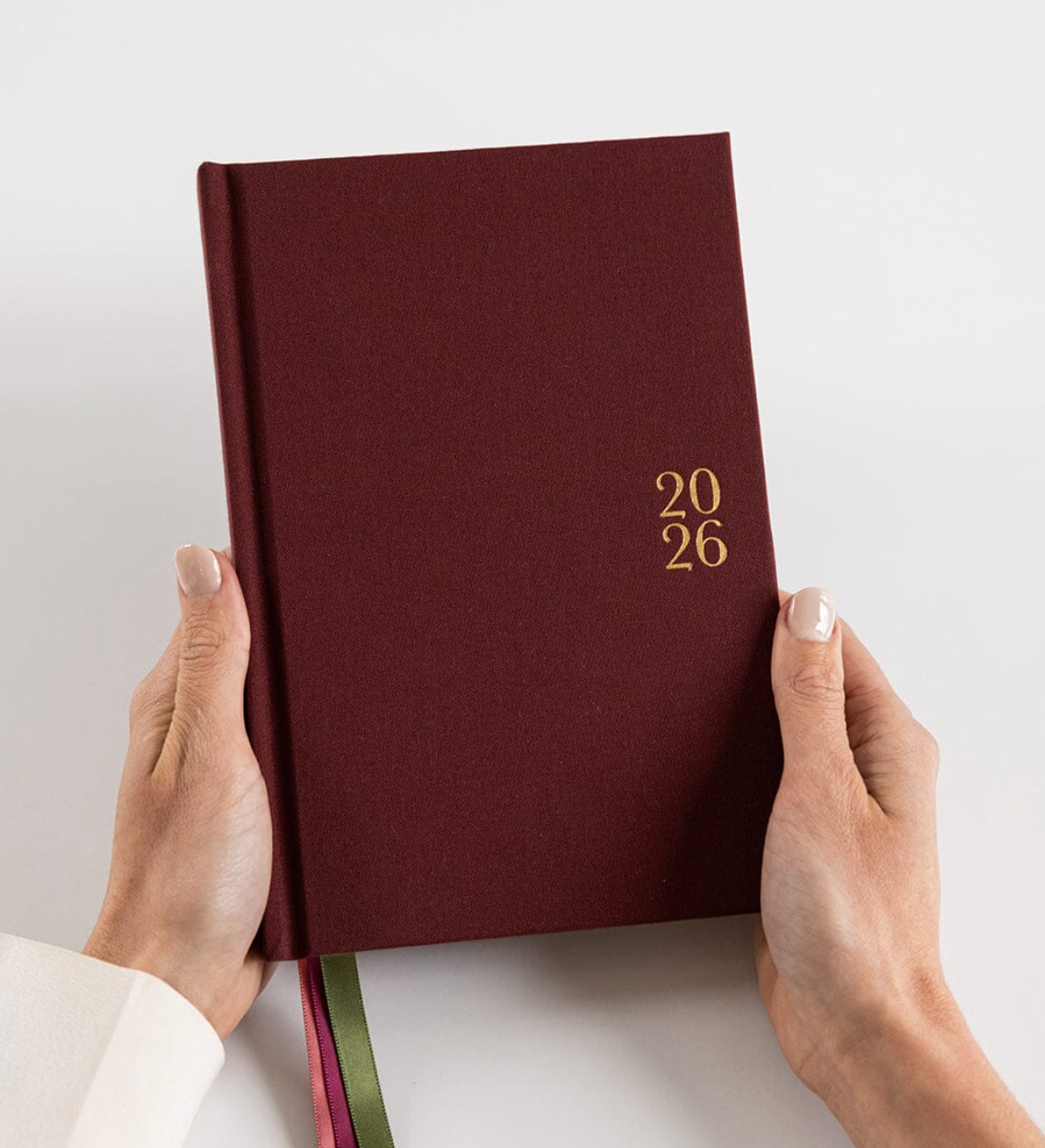 Maroon notebook with '2026' on the cover held by hands against a light background