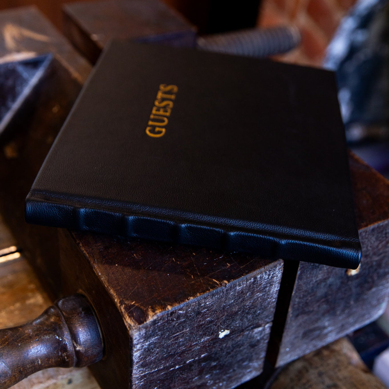 Black leather guest book titled 'GUESTS' on a wooden surface with a blurred background