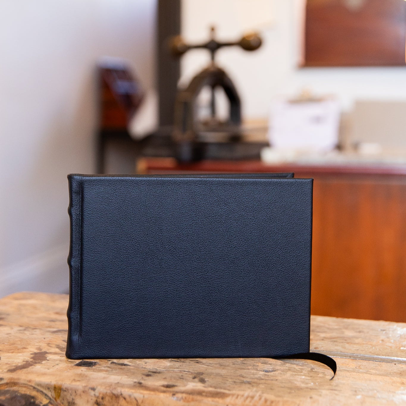 Black leather-bound guest book on a wooden surface with a blurred indoor background