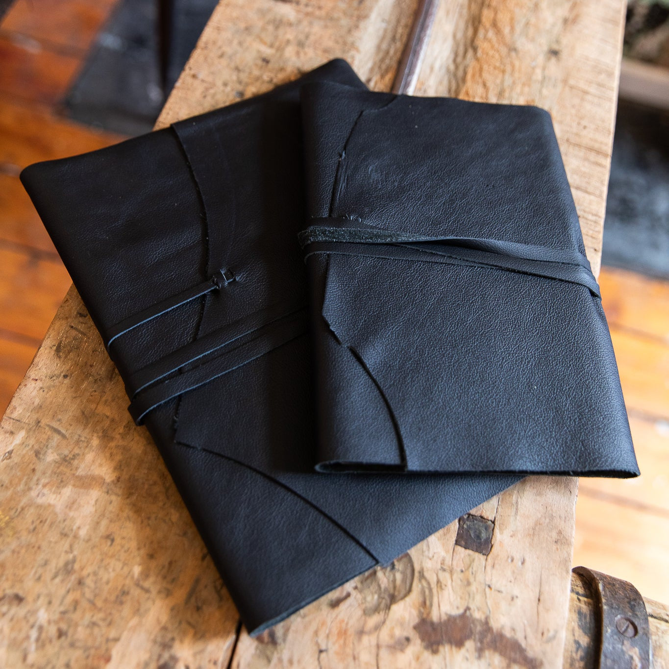 Black leather-bound wrap journals of two sizes on a wooden surface