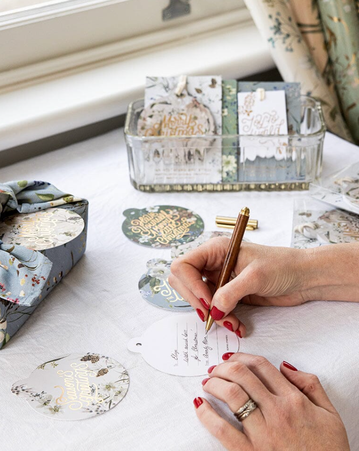 Person writing on a card with decorative elements on a table