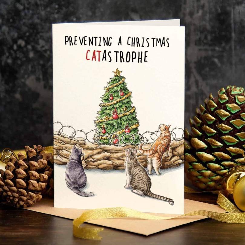 Christmas card with cats and a tree, surrounded by pine cones and ornaments.