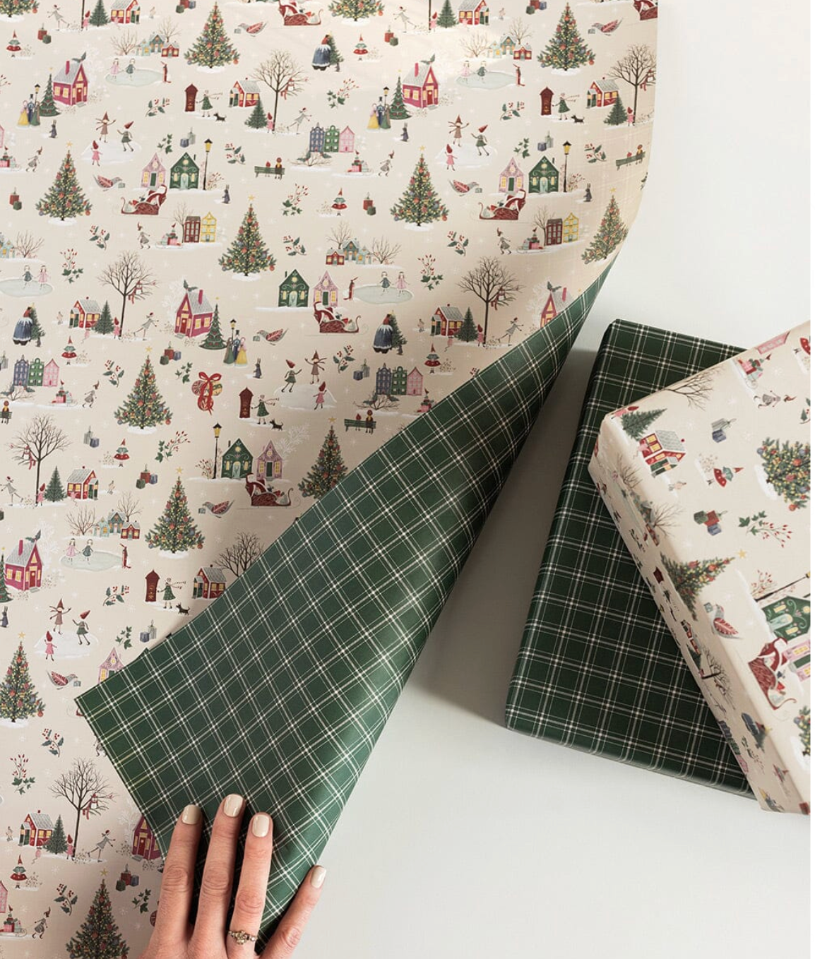 Christmas-themed wrapping paper with a hand holding a green plaid sheet.