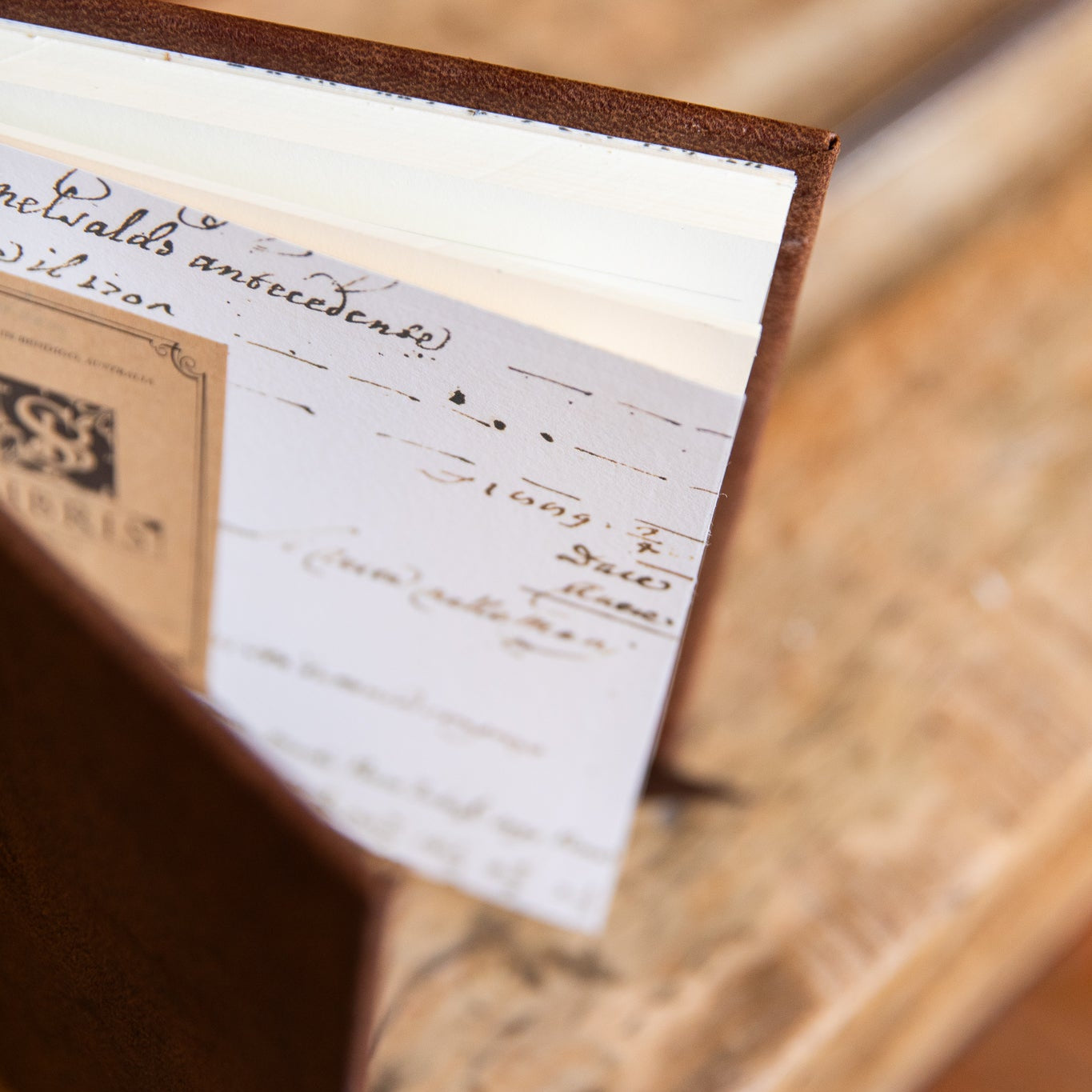 Close-up of a endpapers with cursive writing inside leather book on a wooden surface
