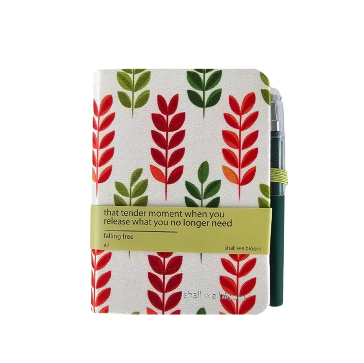A square hardcover journal with a white cover decorated with vertical red and green leaf patterns, wrapped with a yellow-green elastic band that reads 'that tender moment when you release what you no longer need falling free'. A dark green pen is tucked behind it, and the journal is photographed on a clean white background.