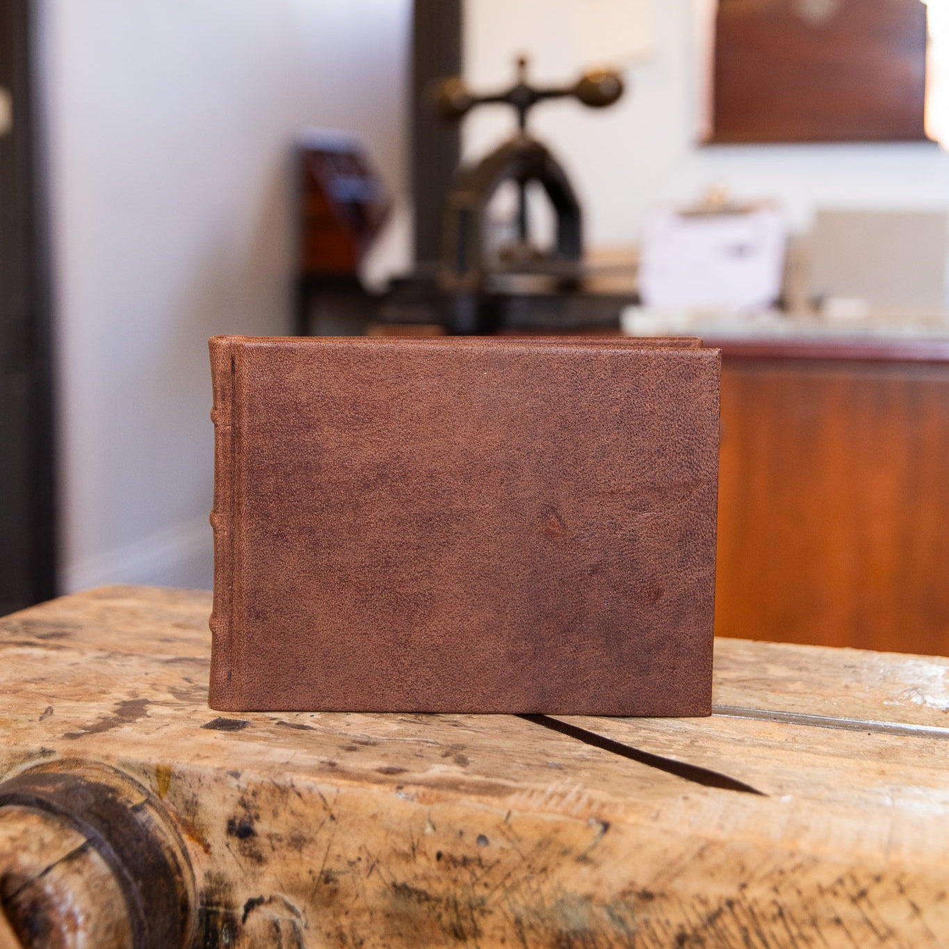 Brown leather-bound book on a wooden surface with a blurred background
