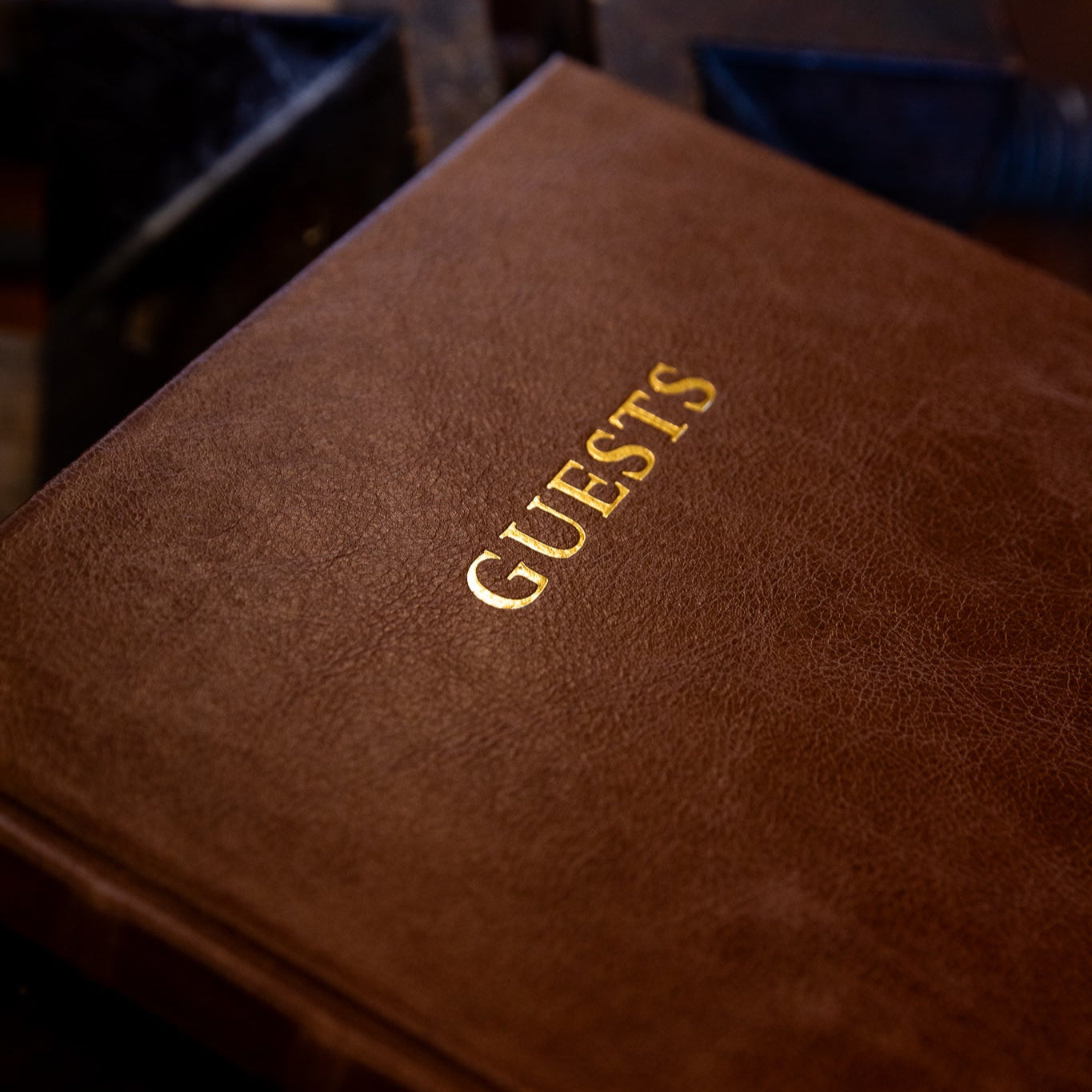 Brown leather guest book with 'GUESTS' embossed in gold on a dark background