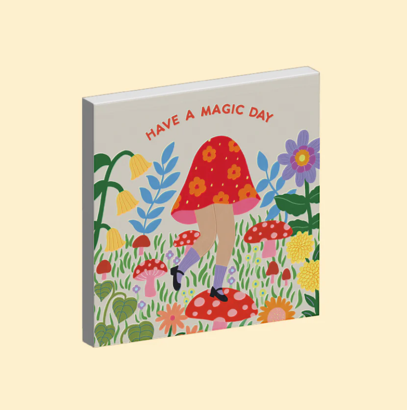 Ceramic magnet with a colourful illustration of a person in a red mushroom dress and, surrounded by flowers and text 'Have a magic day' on a beige background.