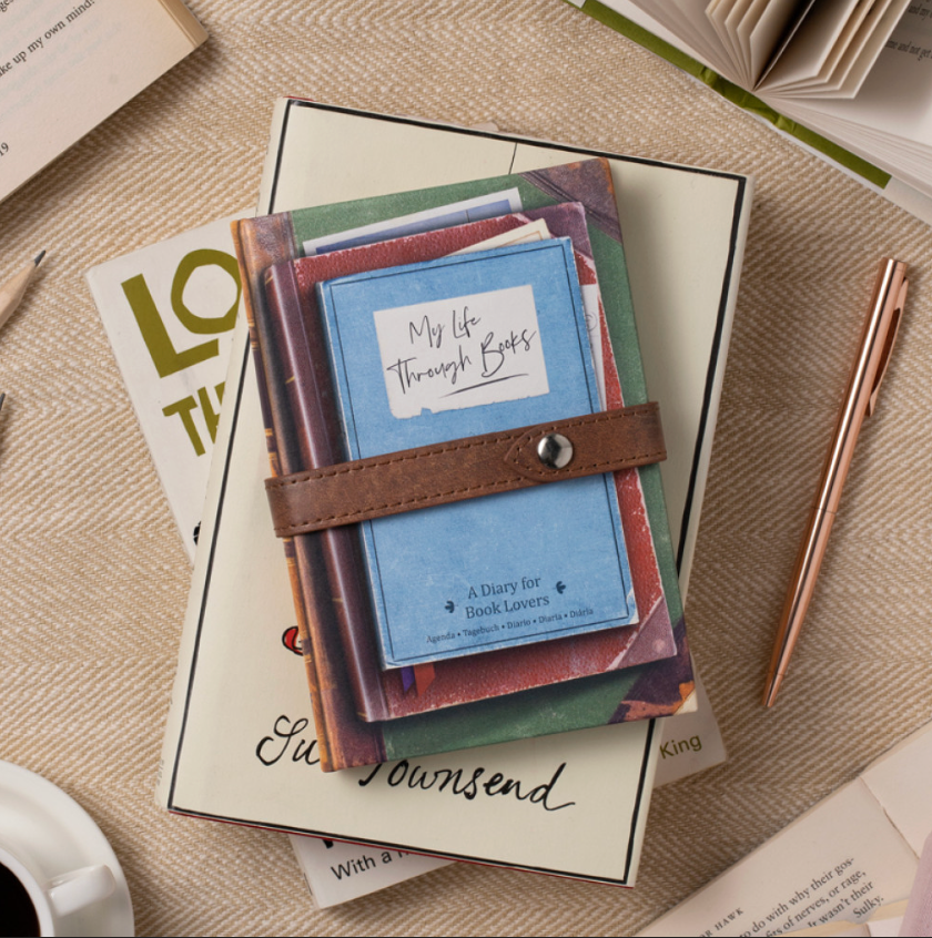 Stack of books with a blue diary on top, surrounded by other books and a pen on a textured surface.
