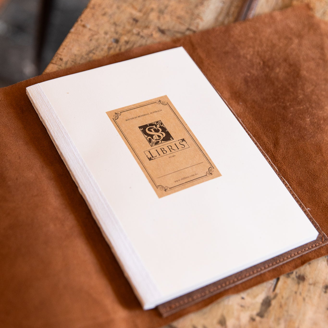 Brown leather-bound book with a cream insert featuring a bookplate on a wooden surface
