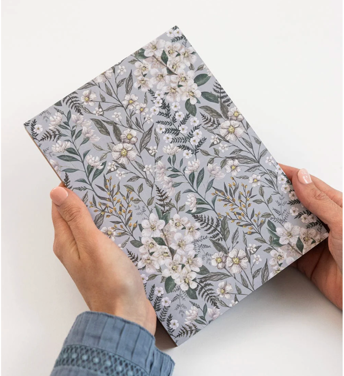 Floral-patterned notebook held by hands on a white background