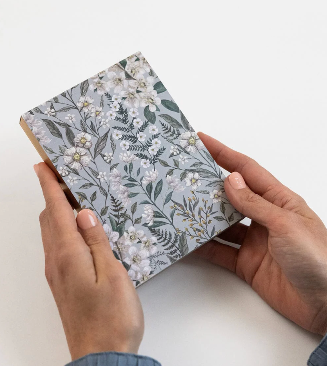 Hands holding a small notebook with floral pattern on a white background