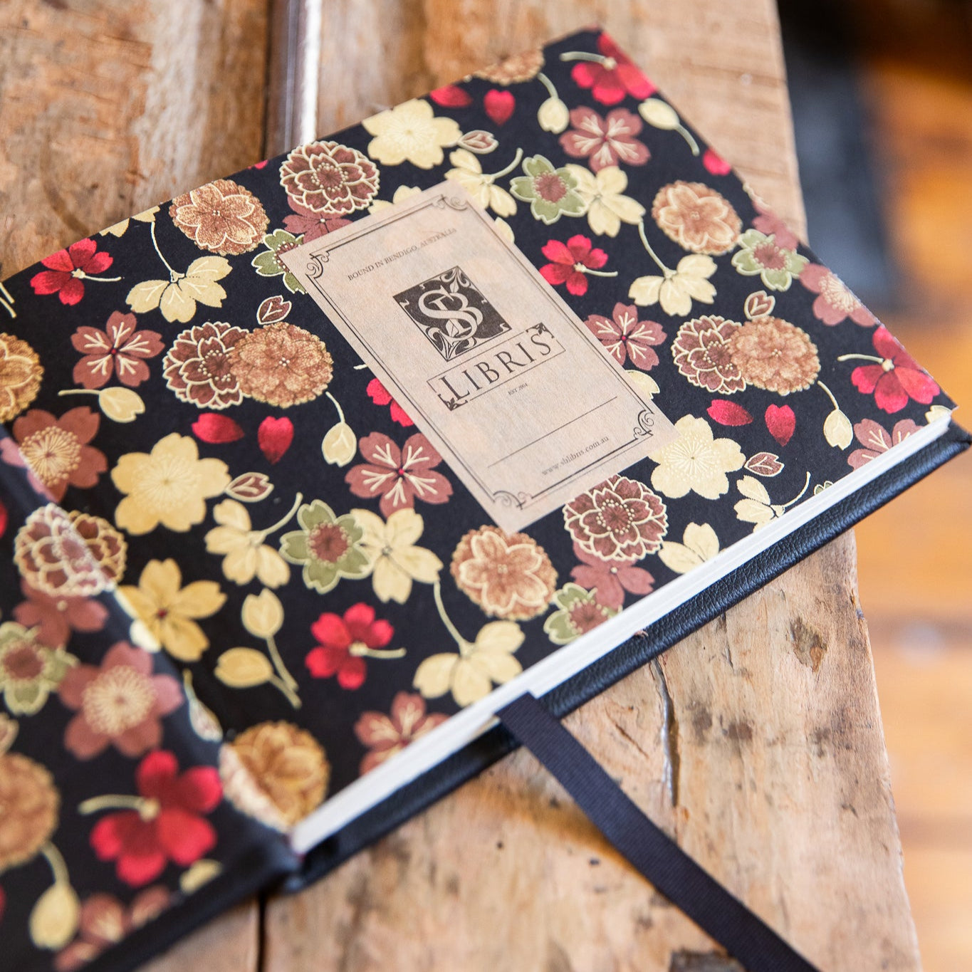 Japanese floral-patterned endpapers with a SB Libris bookplate label on a wooden surface.