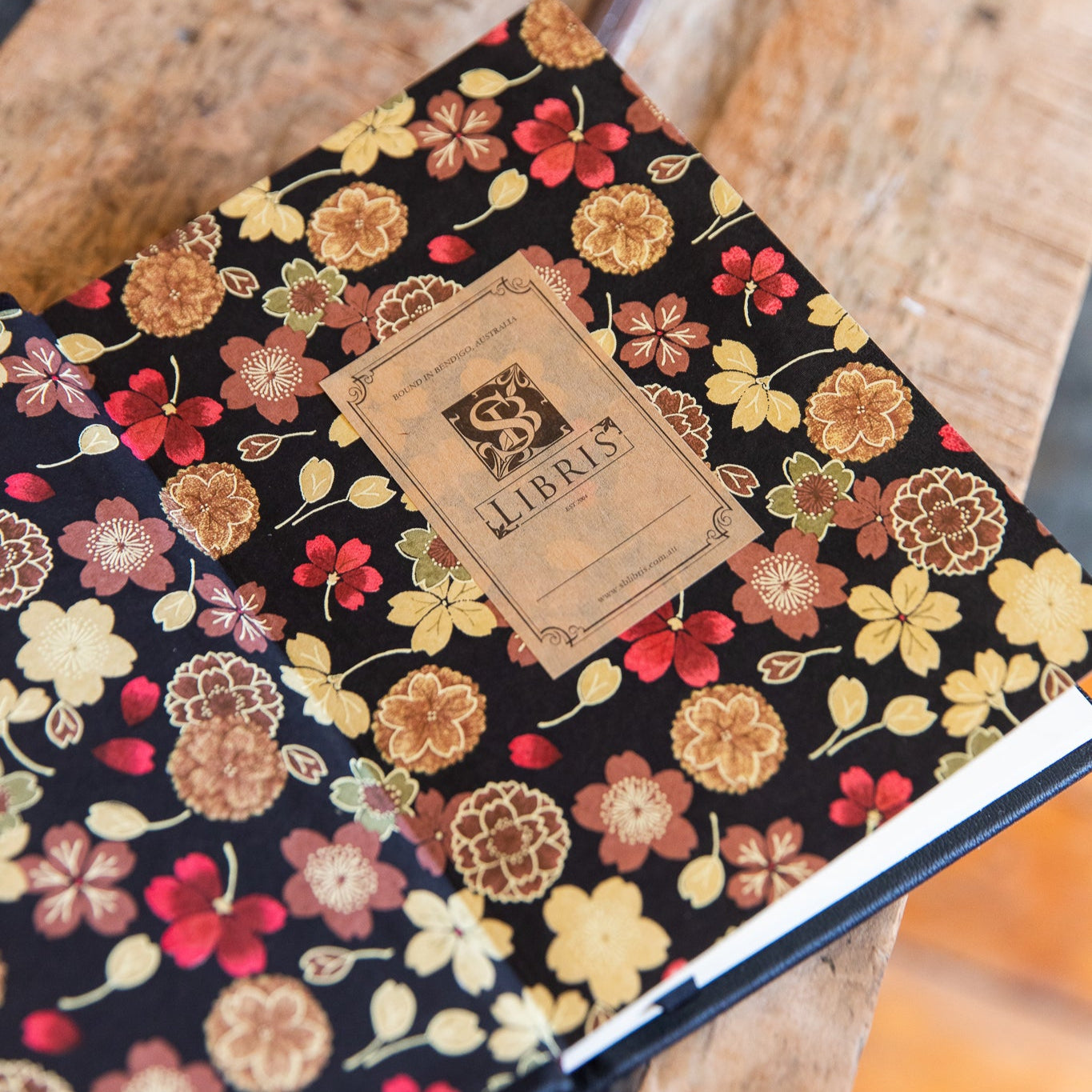 Floral journal endpapers with a visible SB Libris brand bookplates on a wooden surface