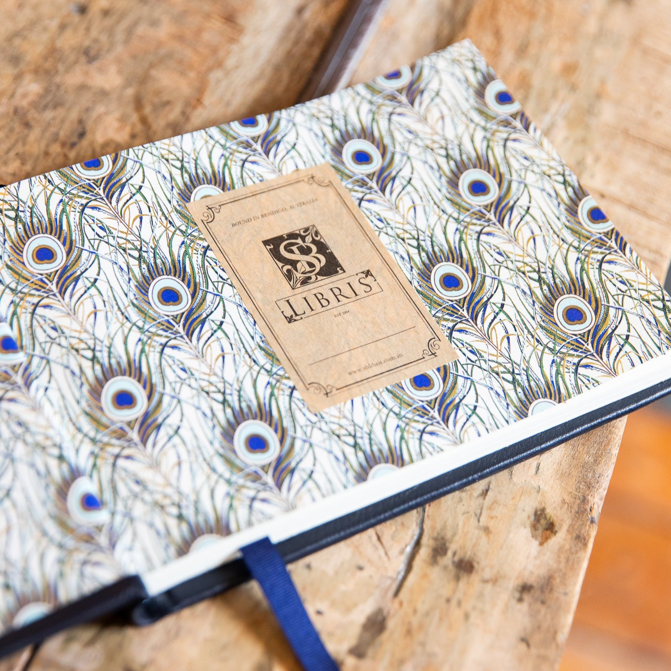 Signature book with peacock feather pattern and a bookplate on a wooden surface