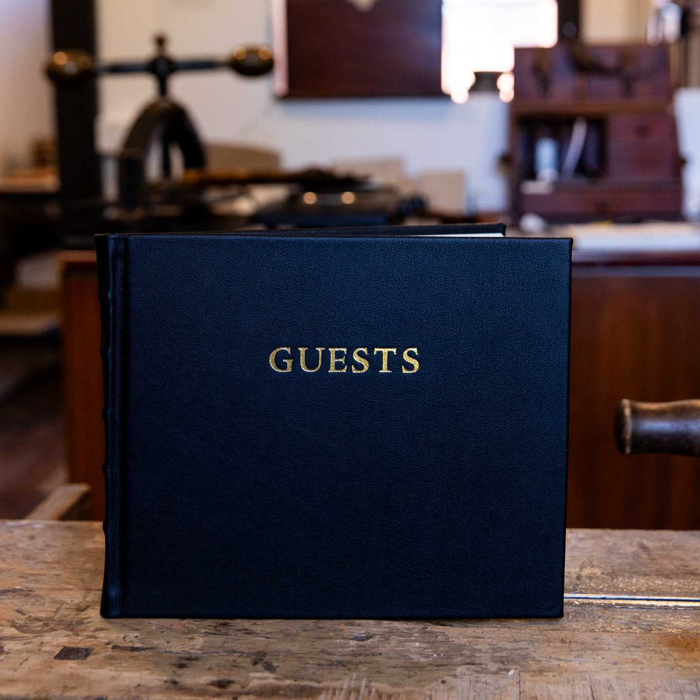 Black leather book titled 'GUESTS' on a wooden surface with a blurred background