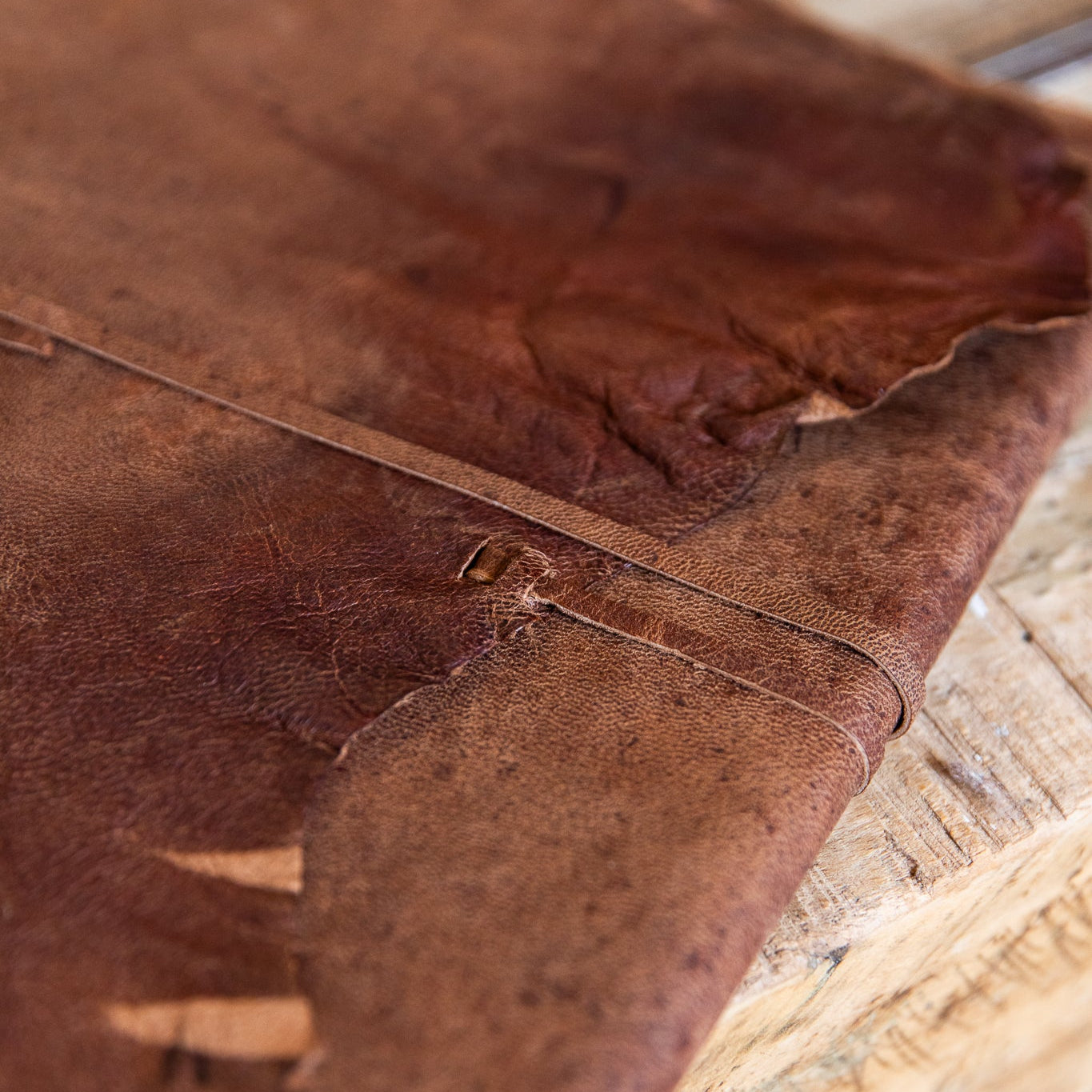 Close-up of a brown leather book with visible stitching on a wooden surface.