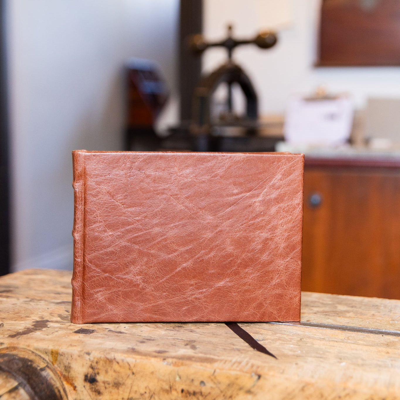 Brown leather-bound guest book on a wooden surface with a blurred bindery background