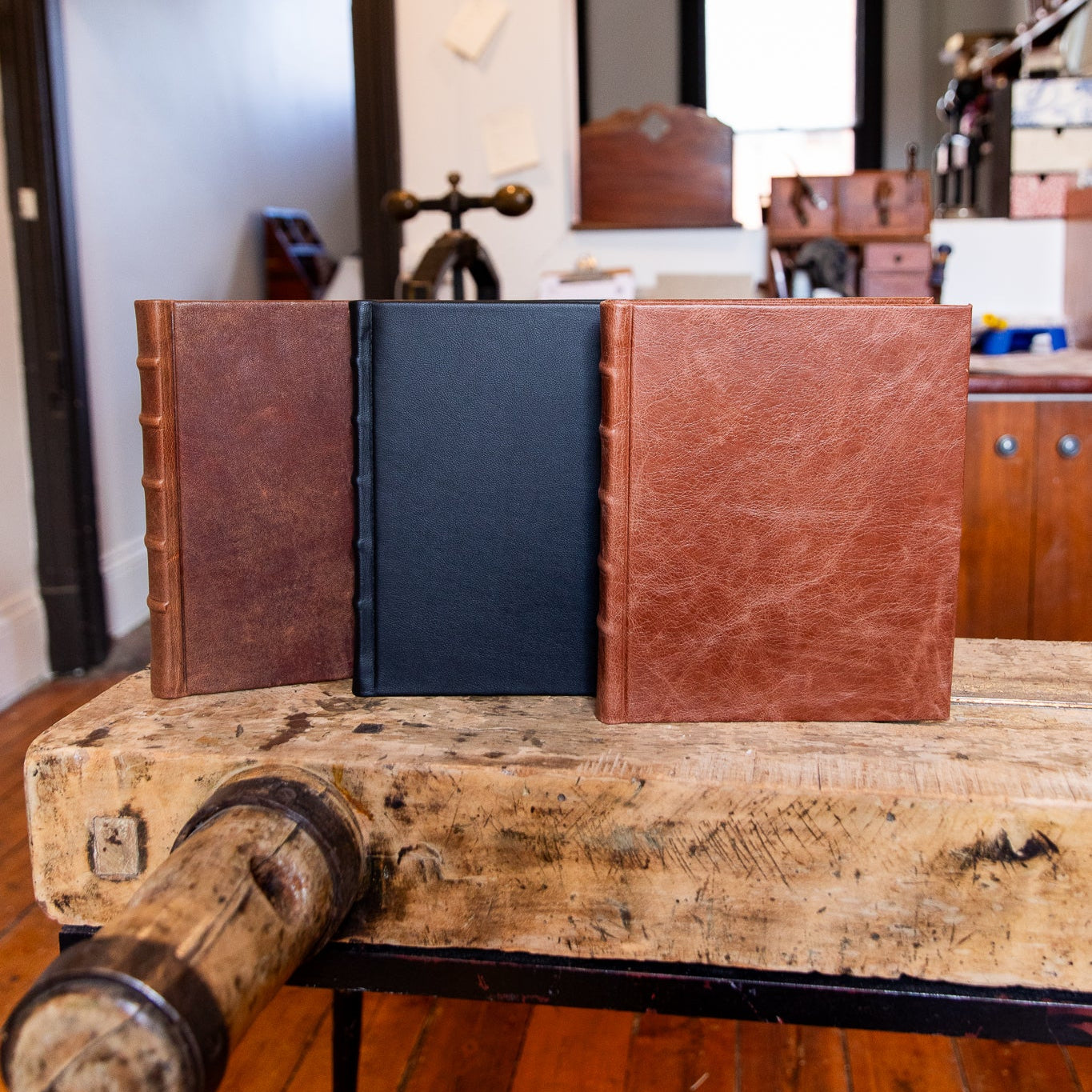 Three books with leather covers on a wooden surface in a room.