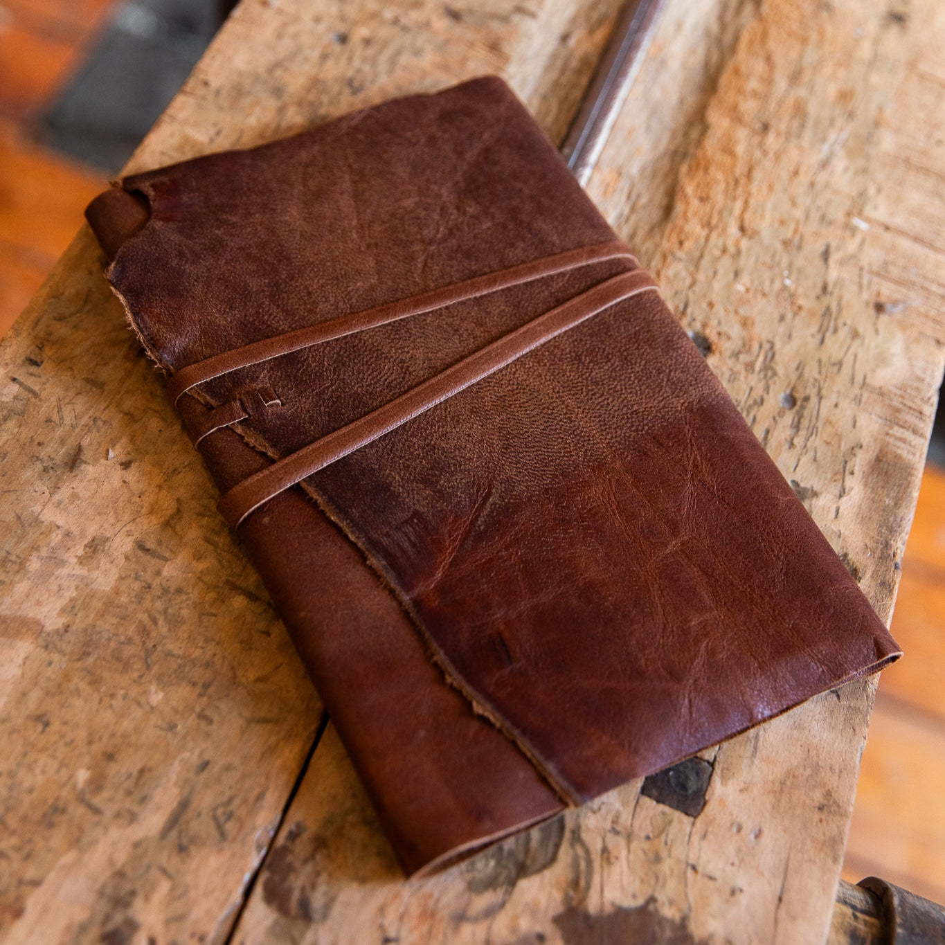 Leather refillable wrap journal in aged goatskin on a wooden press