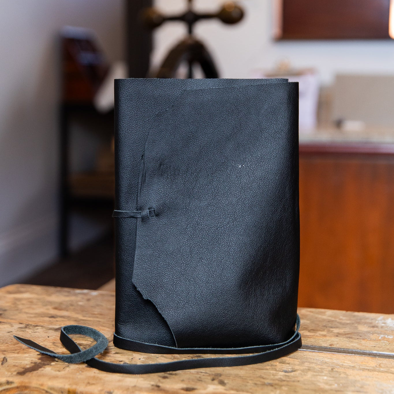 Black leather journal on a wooden surface with a blurred bindery background