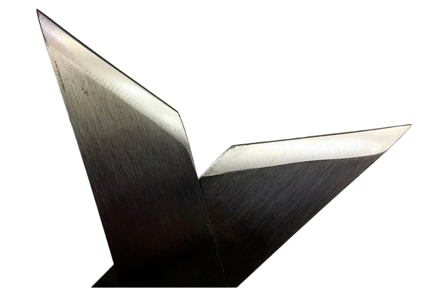A close-up studio shot of a metallic V-shaped object, likely a machined metal blade or bracket, showing a brushed silver-to-black finish and sharp beveled edges, isolated on a white background.