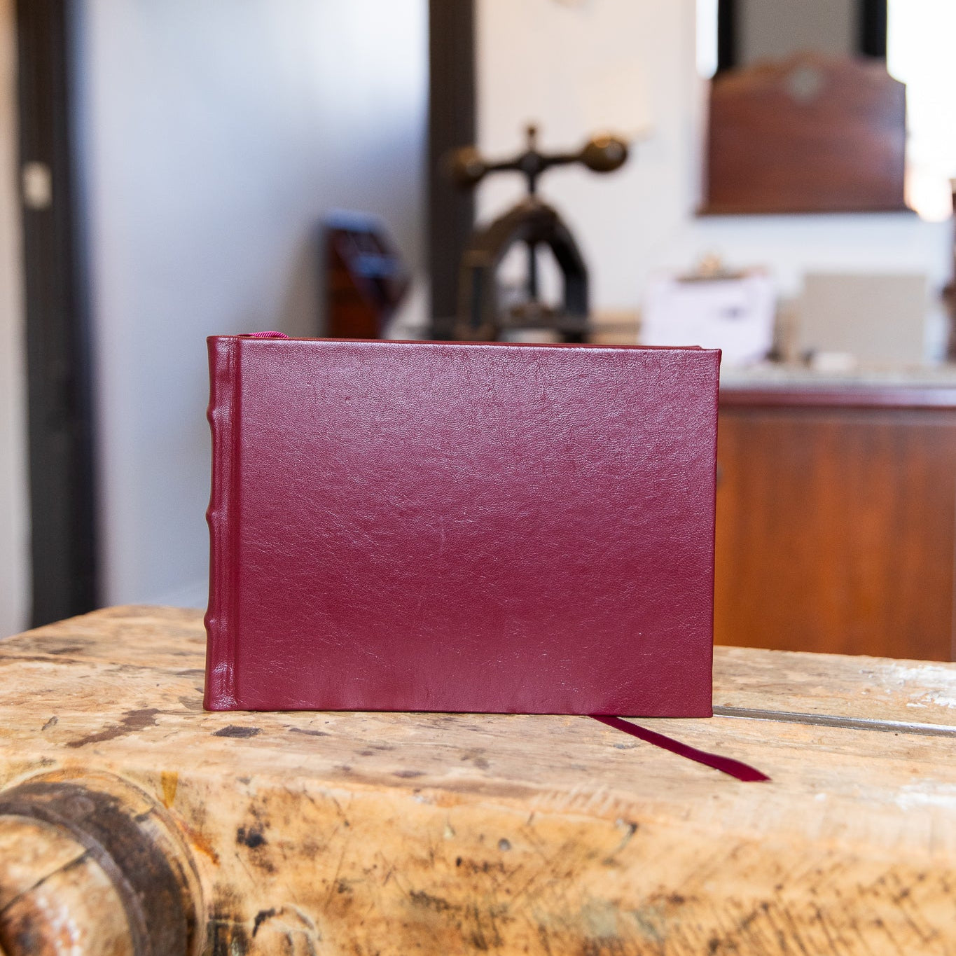Maroon leather-bound book on a wooden surface with a blurred indoor background