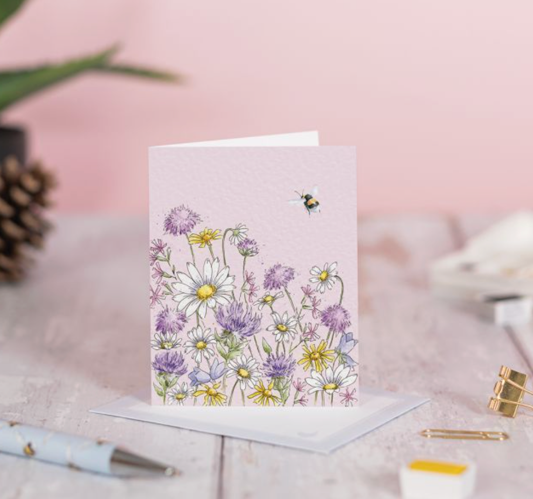 Greeting card with floral design and bee on a pink surface