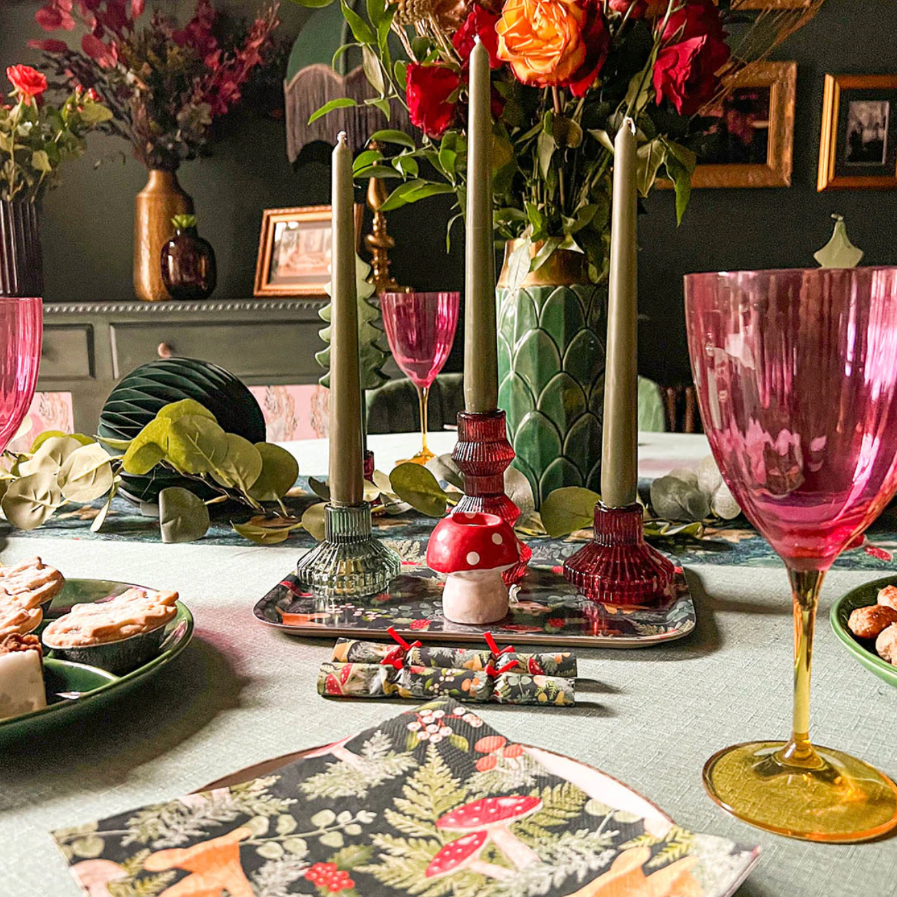 Decorative table setting with pink glasses, candles, and floral arrangements.