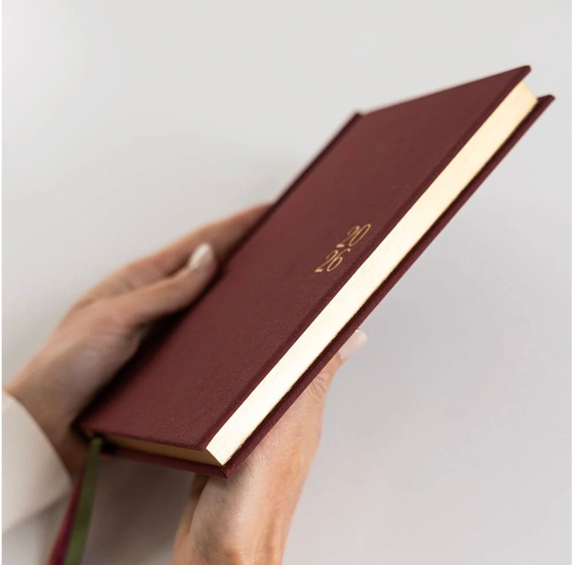 Hand holding a red linen-bound book with gold edges on a light gray background