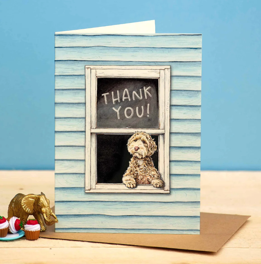 Greeting card with a dog sitting in a window frame and 'Thank You!' on a chalkboard, against a blue striped background.