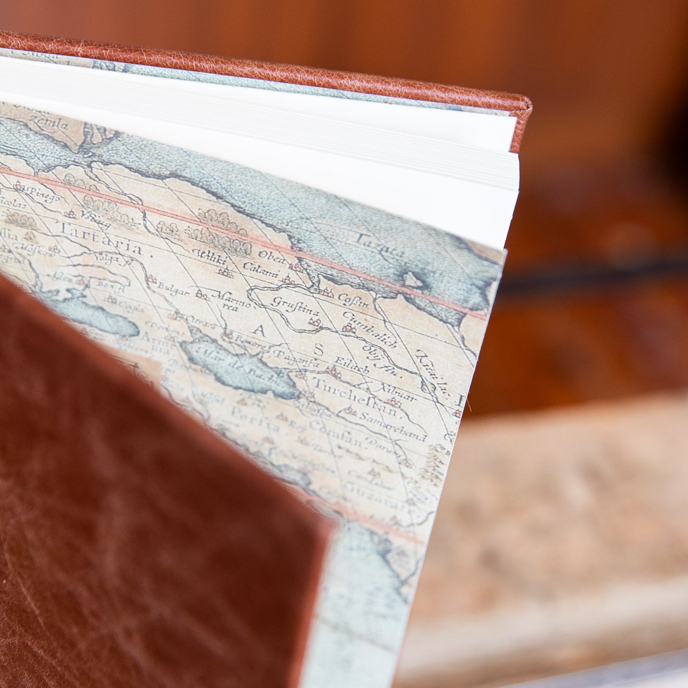 Close-up of a leather-bound book with a vintage map on the endpapers, blurred background