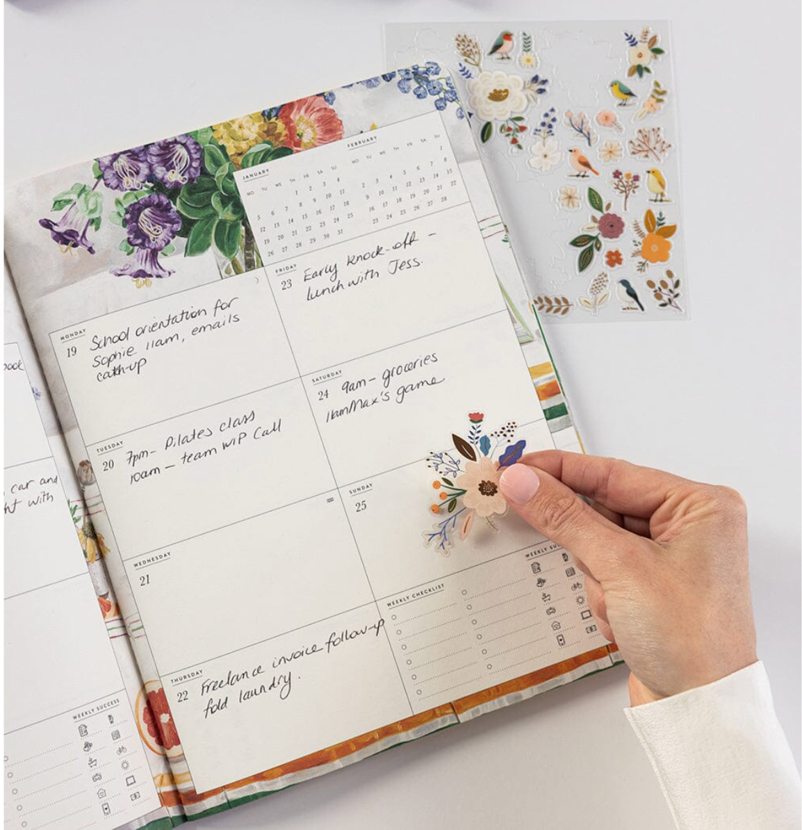 Hand holding a planner with floral stickers on a white surface