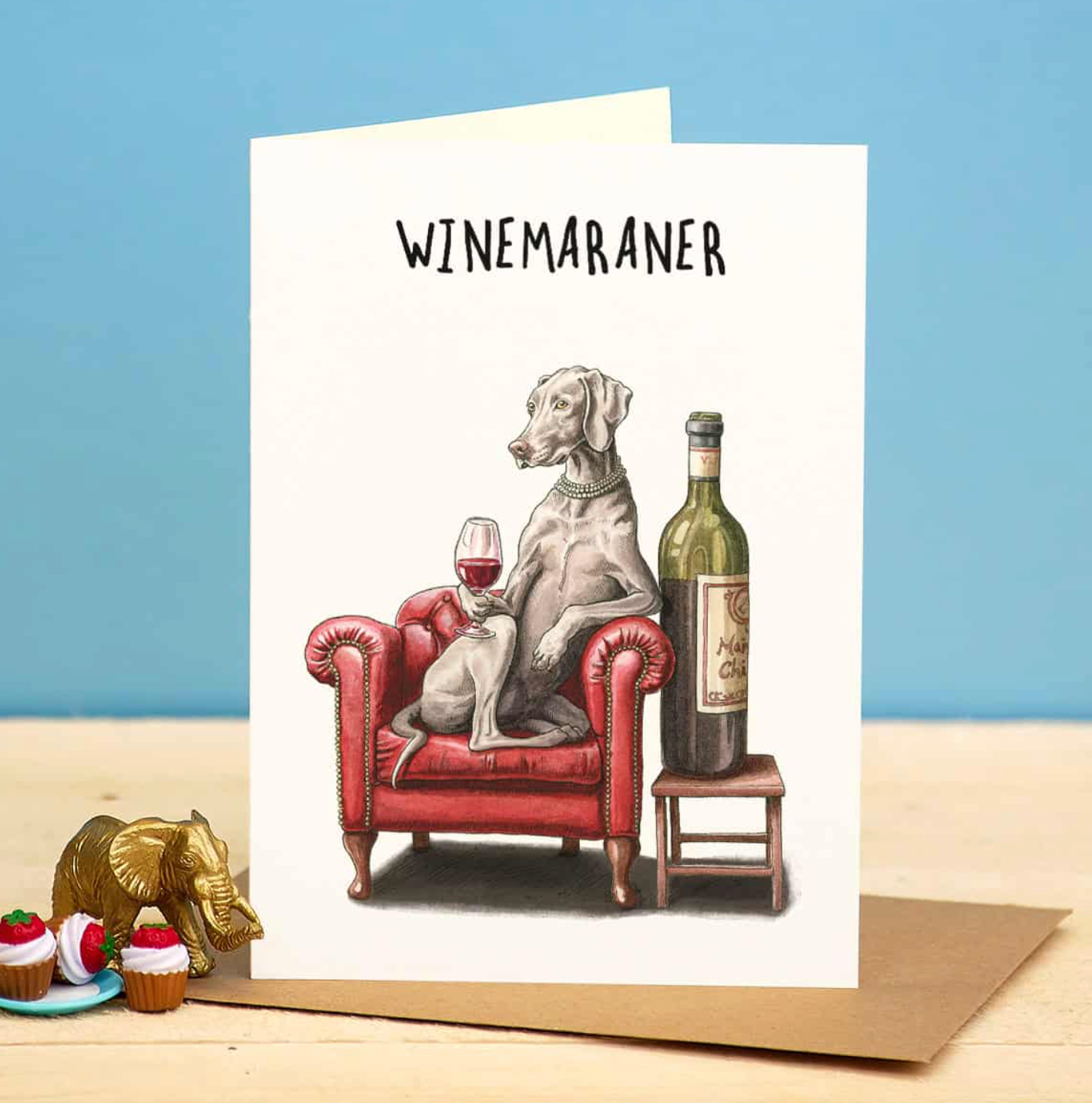 Card with a dog sitting on a red armchair with wine, labeled 'WINEMARANER', on a blue background.