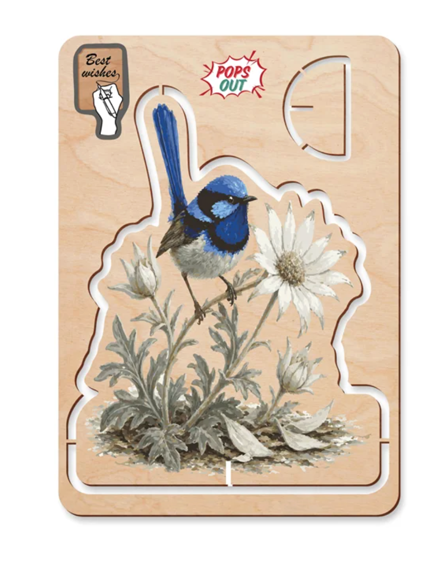A wooden pop our card with a bird and flower design, shown on a light wood background. The puzzle features a blue and white bird perched on a white flower with gray-green foliage.