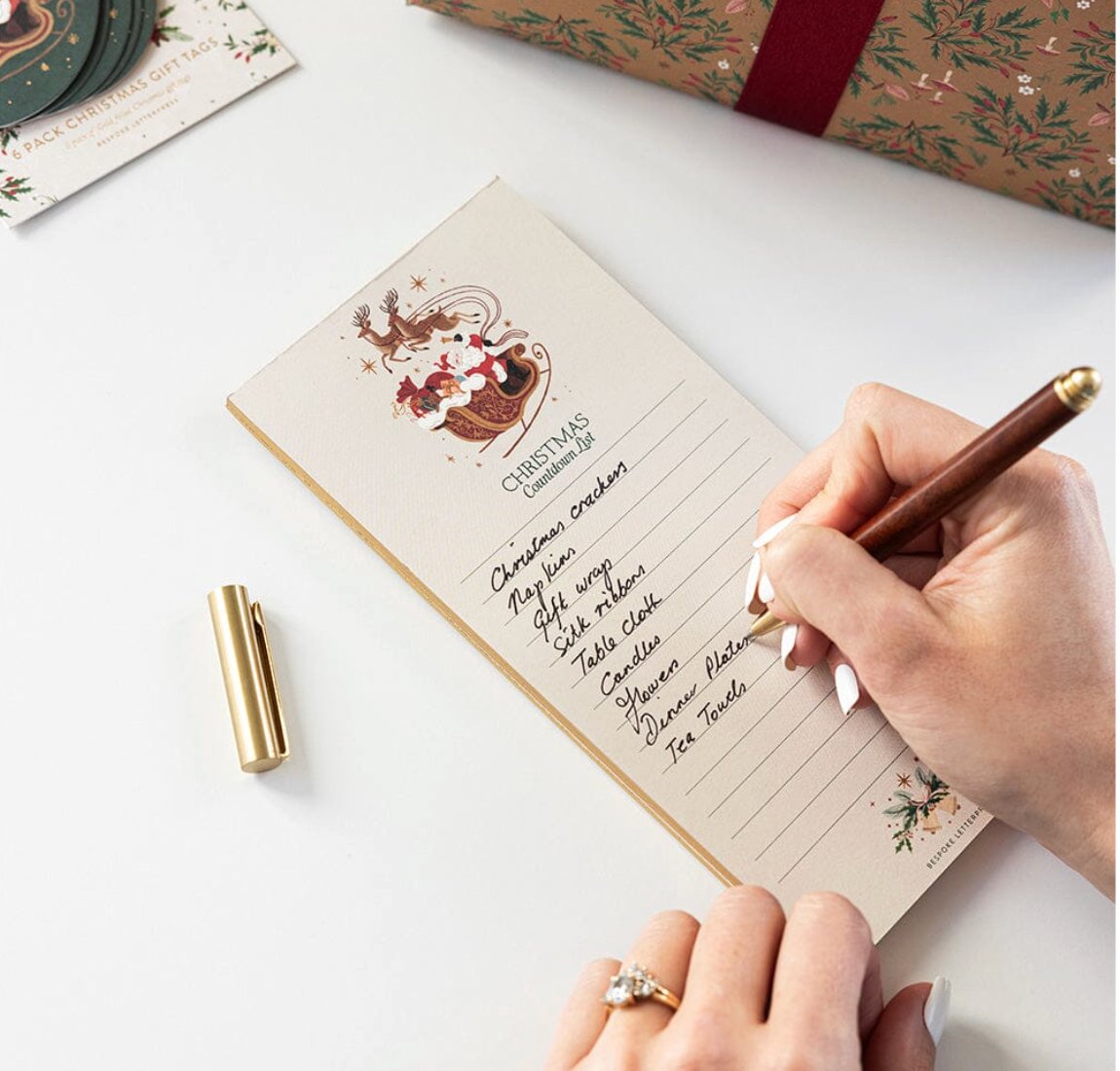 Hand writing on a Christmas-themed notepad with a pen, surrounded by festive wrapping paper.