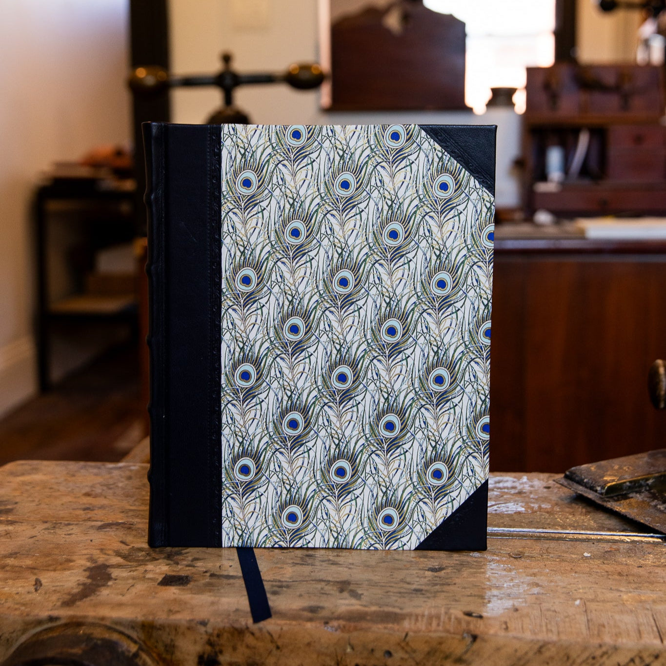 Front view of the large SB Libris half leather journal featuring decorative peacock feather paper and navy leather binding.