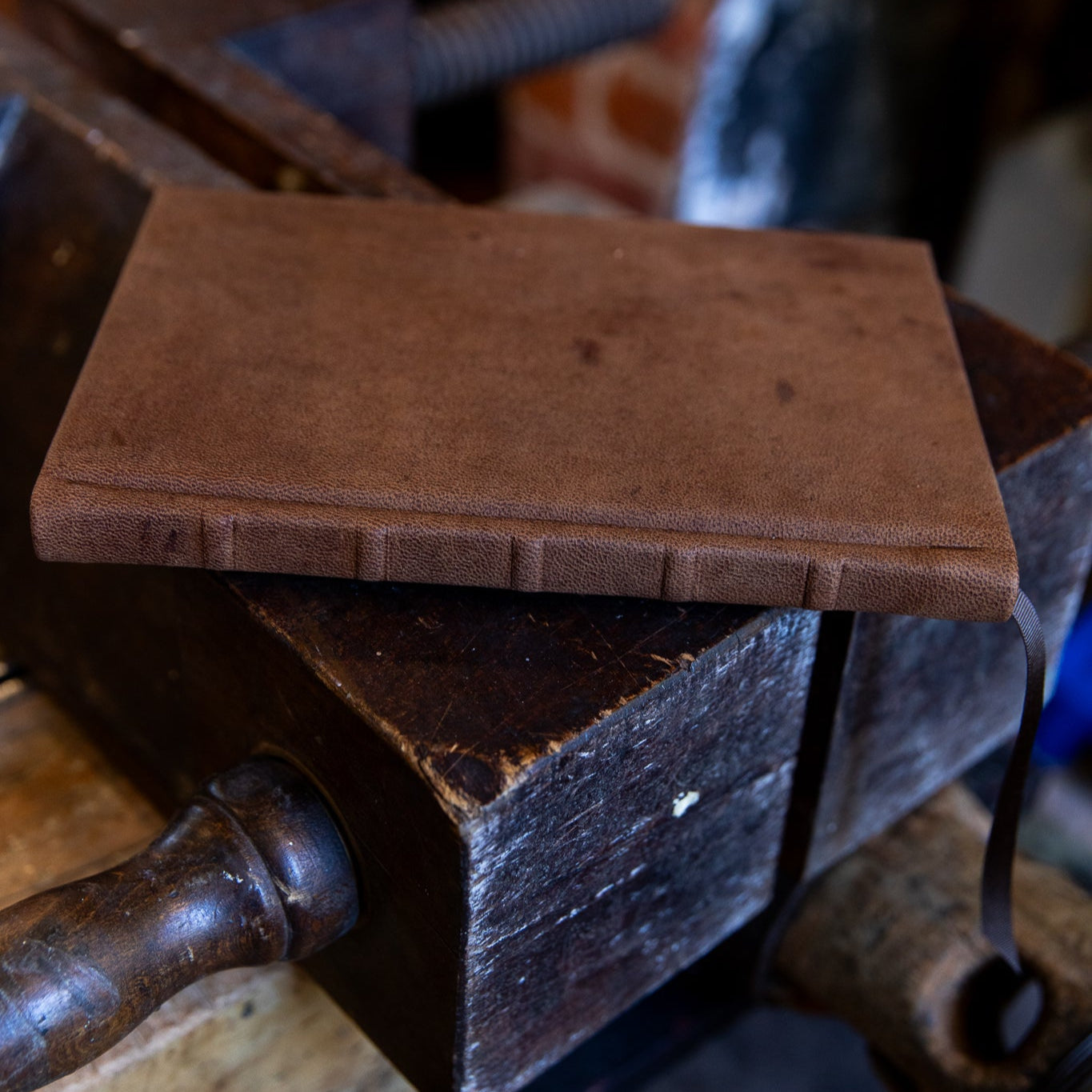 A horizontal view of the aged goatskin full leather journal resting on a vintage bookbinding finishing press, highlighting the supple leather texture and raised bands on spine.