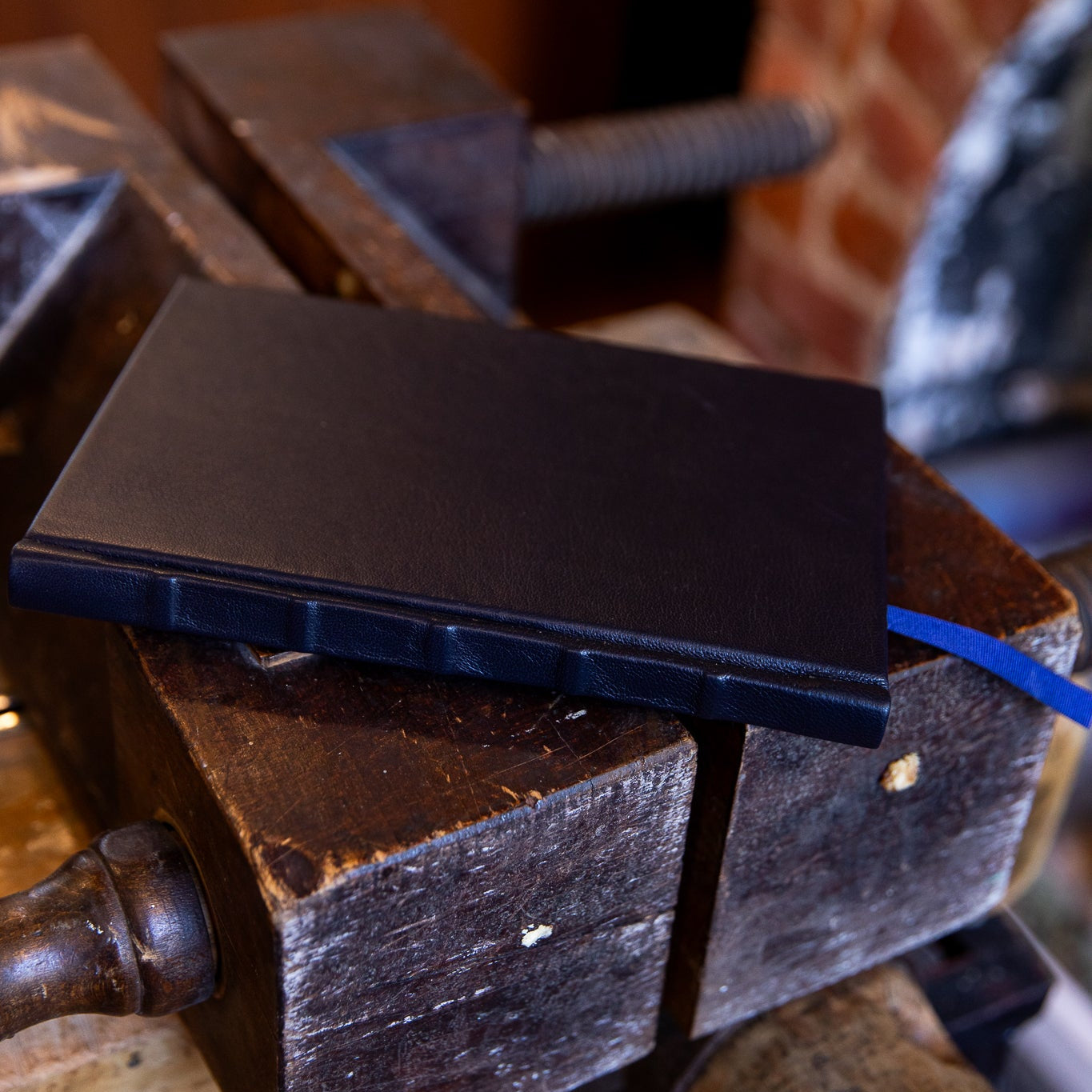 Black leather SB Libris journal resting flat across a traditional bookbinding finishing press, showing natural sheen and raised band spine detail.