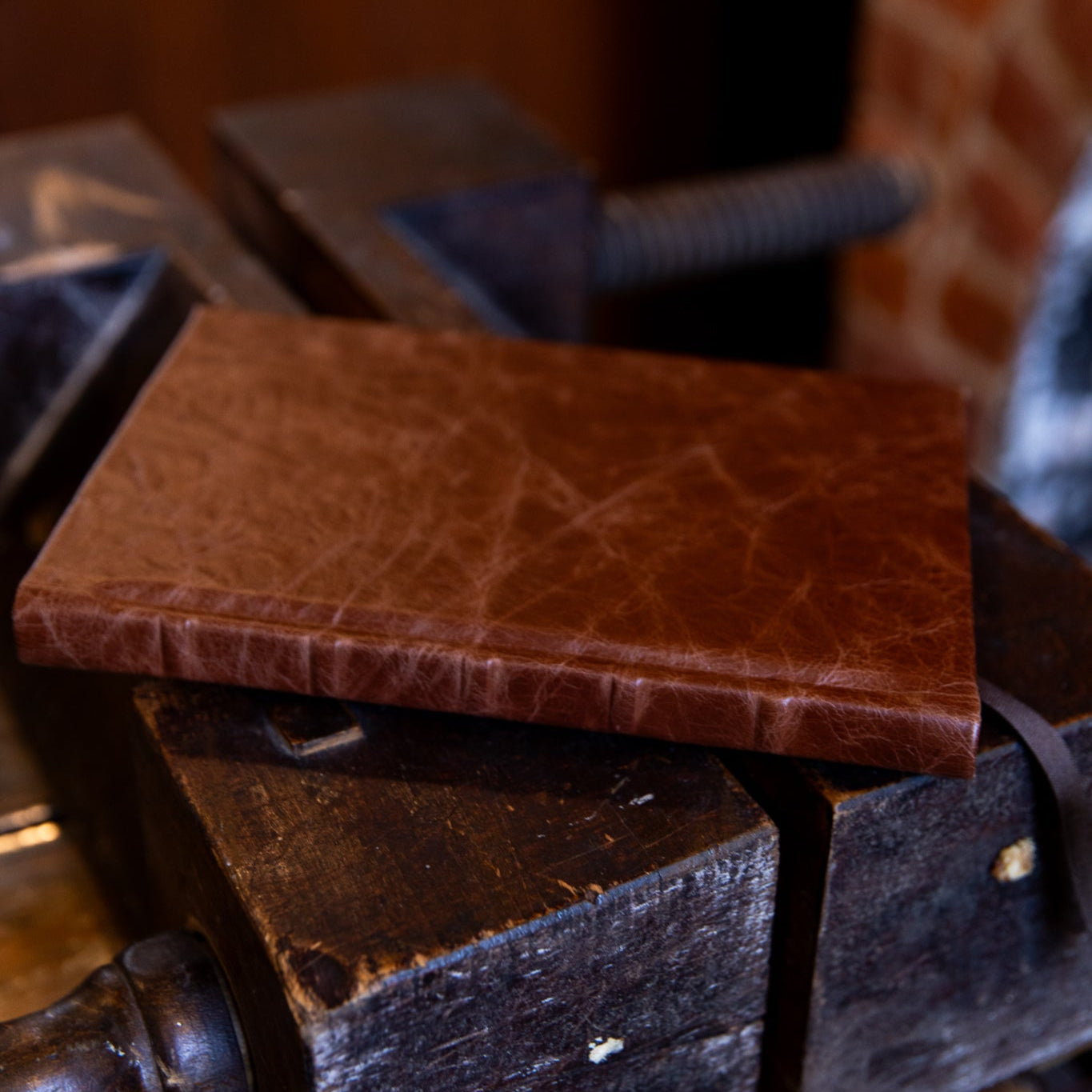 Chestnut leather SB Libris journal laid flat across a traditional bookbinding finishing press, showing natural creases and hand-finished spine.