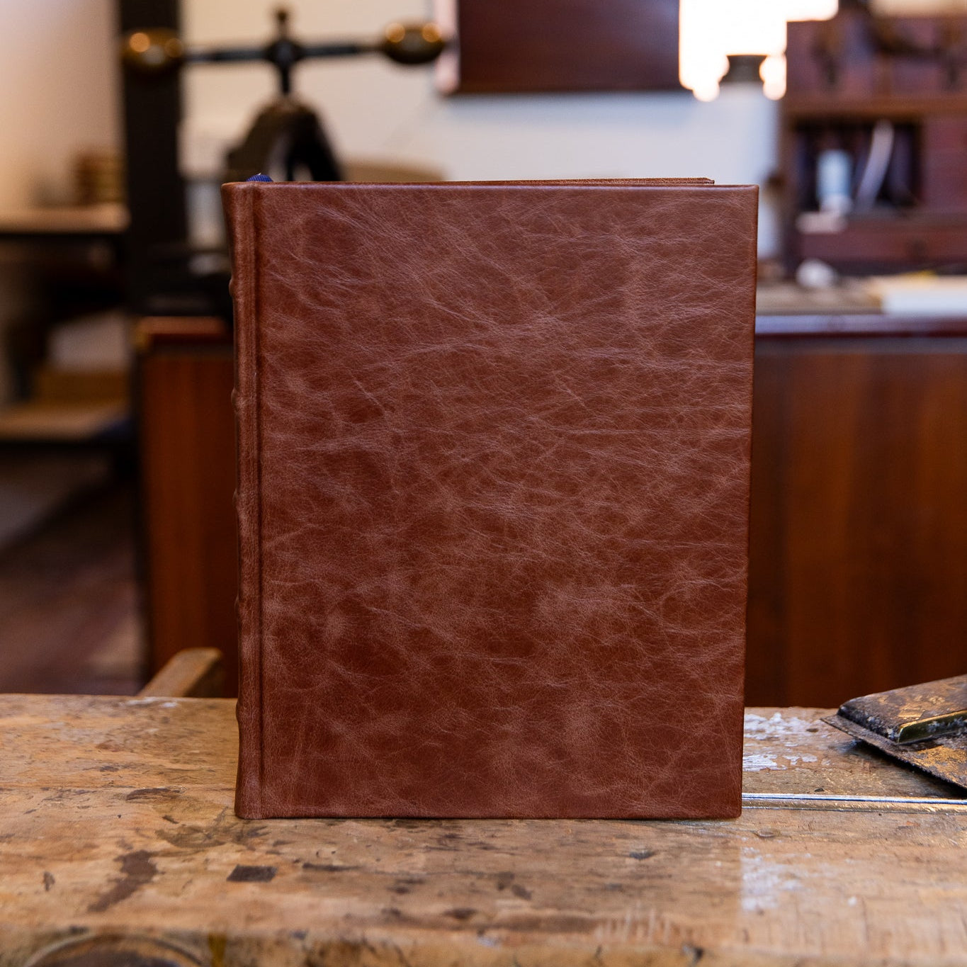 Front view of the large SB Libris Classic Journal in chestnut leather, upright on a wooden bench with rich texture and natural markings.