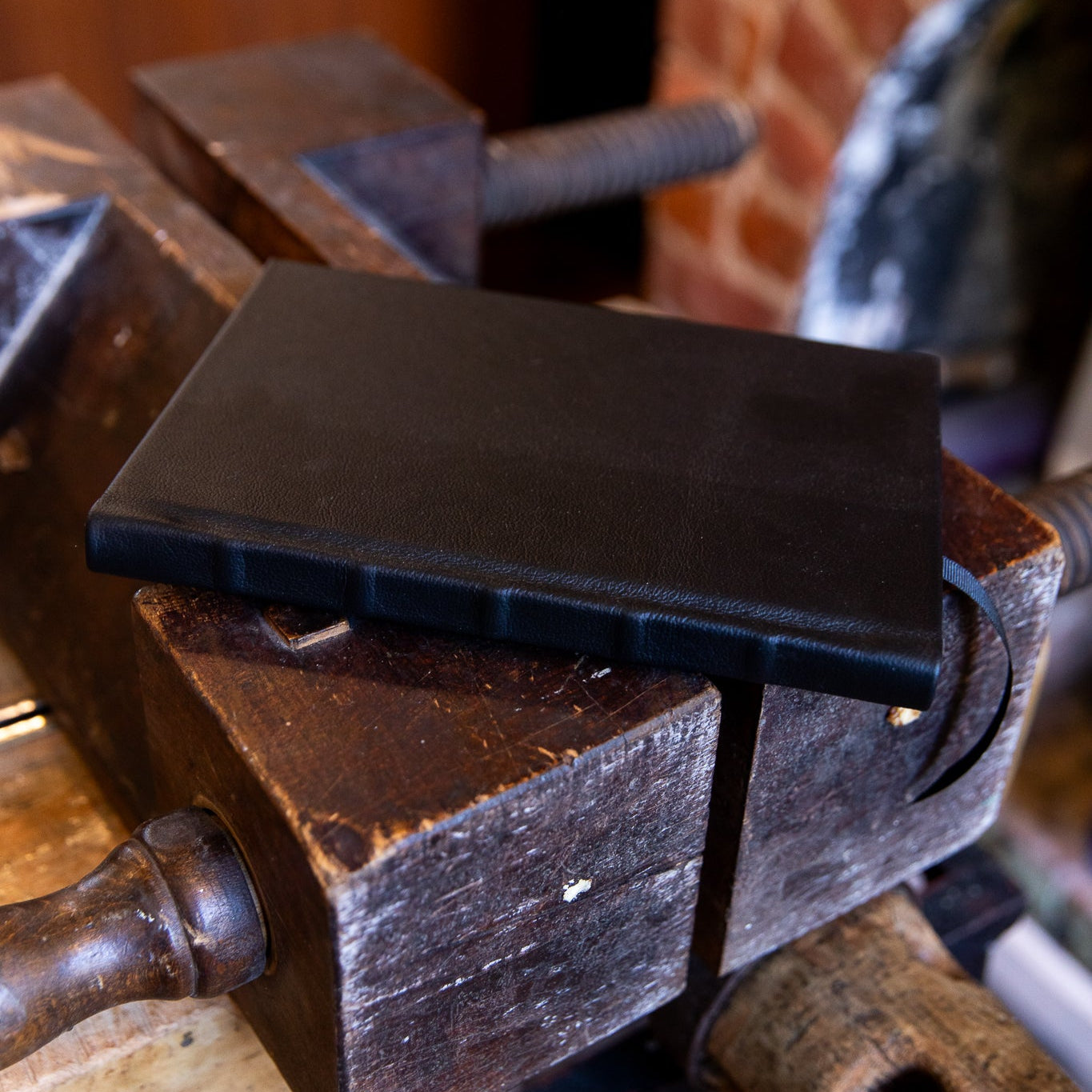 Navy SB Libris full leather journal lying flat across a vintage bookbinding laying press, showing natural leather grain and raised spine bands.