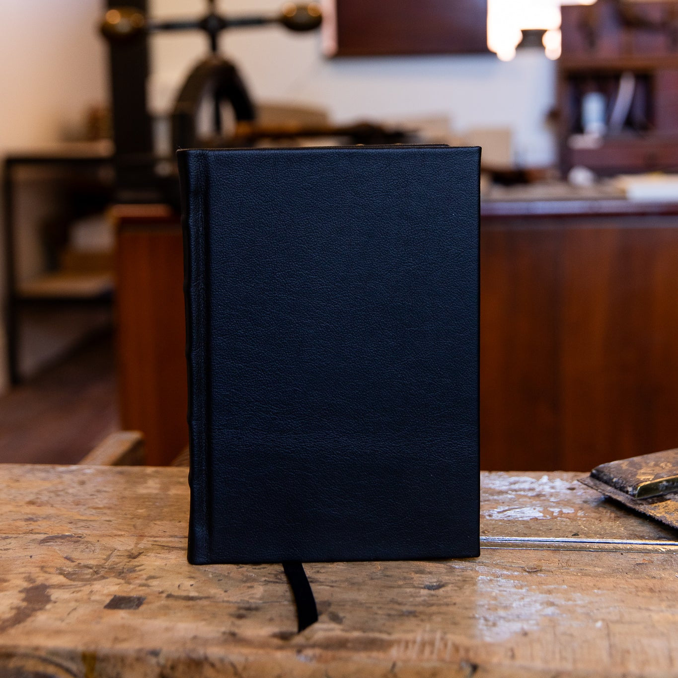 Small navy SB Libris leather journal standing upright on the workbench, featuring subtle spine detailing and a soft matte finish.
