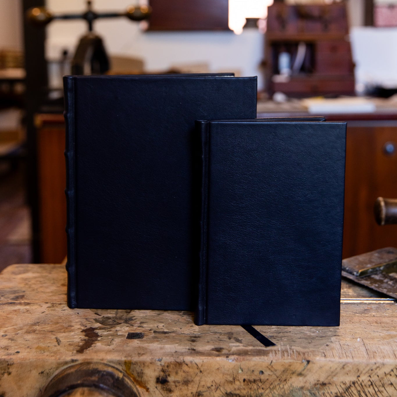 SB Libris Classic Full Leather Journals in black leather, large and small sizes side by side on a wooden workbench with black ribbons.
