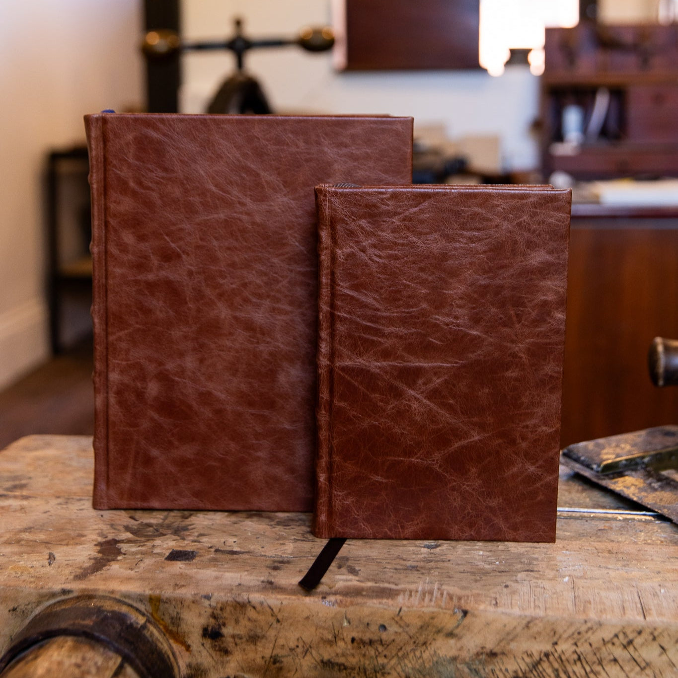 SB Libris Classic Full Leather Journals in chestnut leather, large and small sizes displayed together on a vintage workbench with dark brown ribbons.