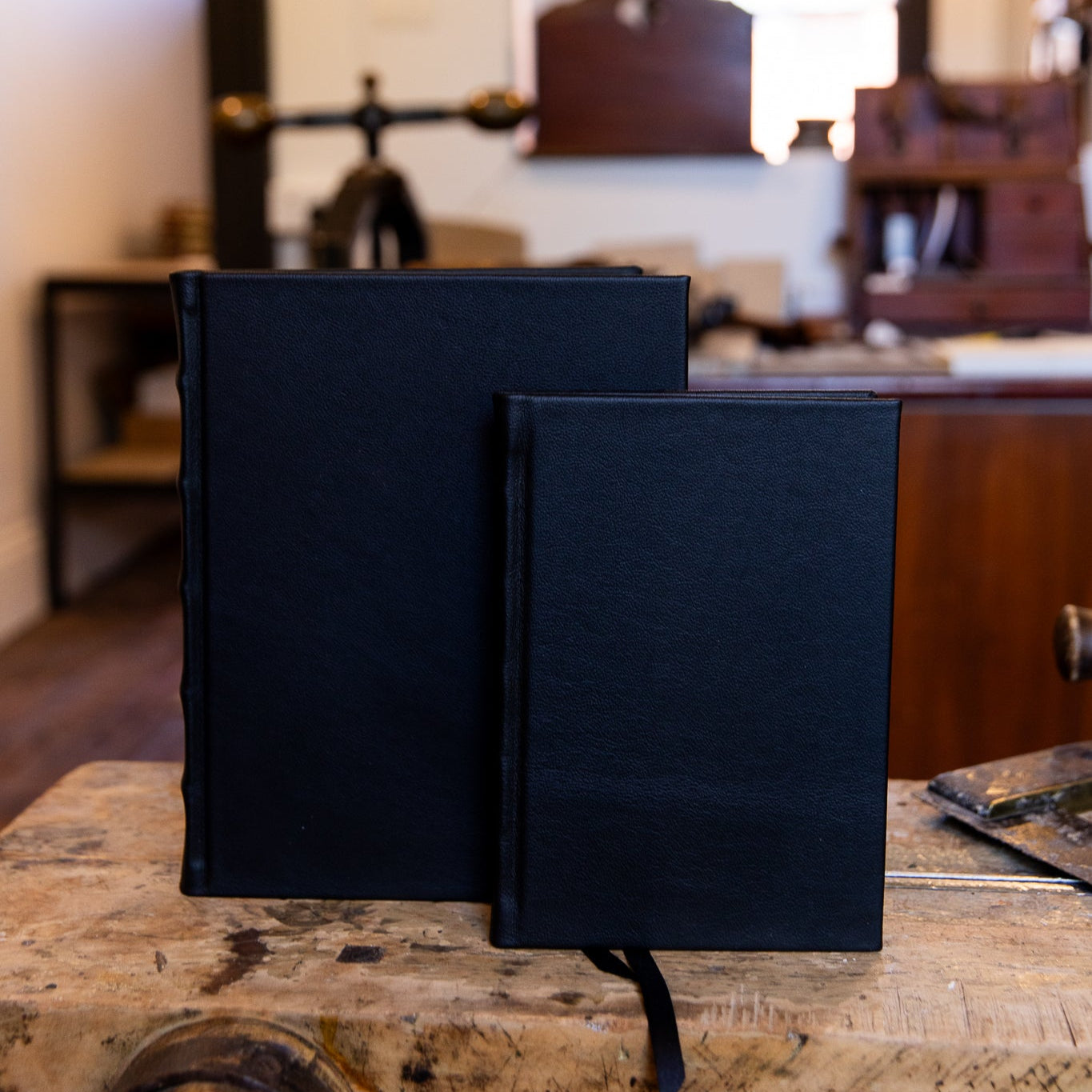 Large and small SB Libris Classic Full Leather Journals in navy leather, side by side on a wooden laying press with matching ribbon markers.