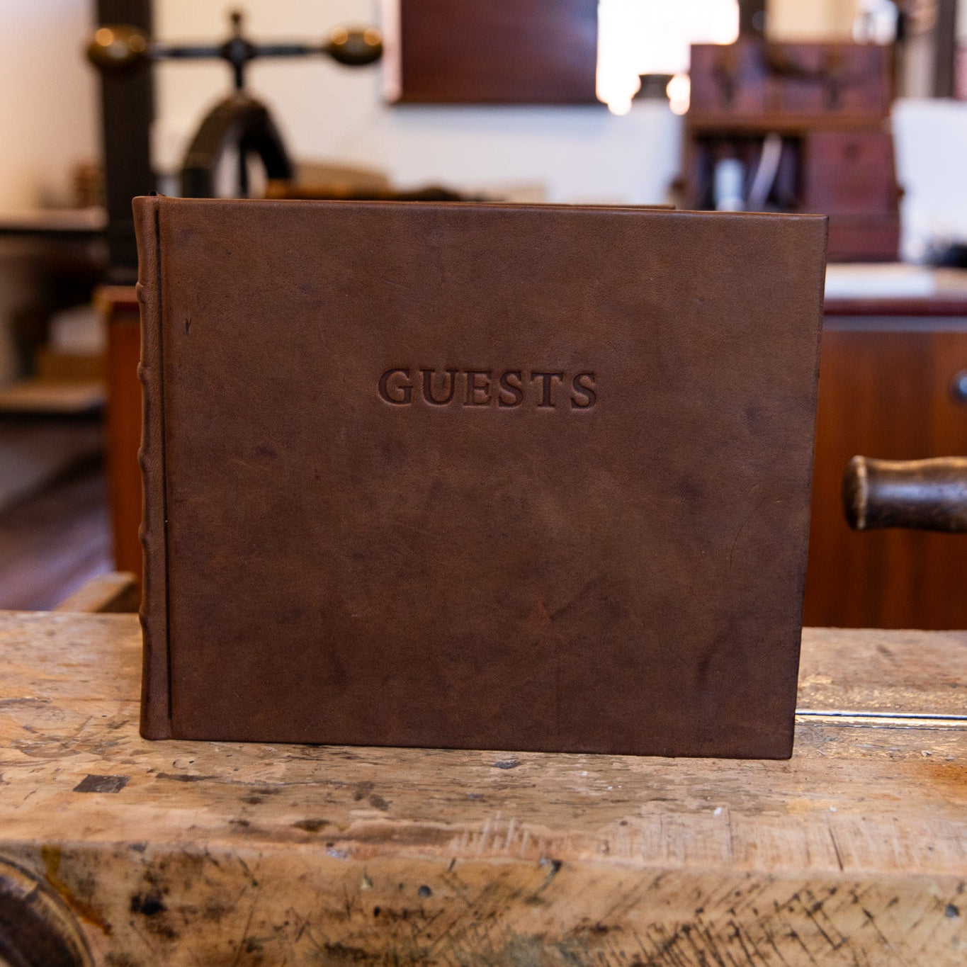 SB Libris full leather guest book in aged goatskin, standing upright on a workbench with the word “GUESTS” blind embossed on the cover.