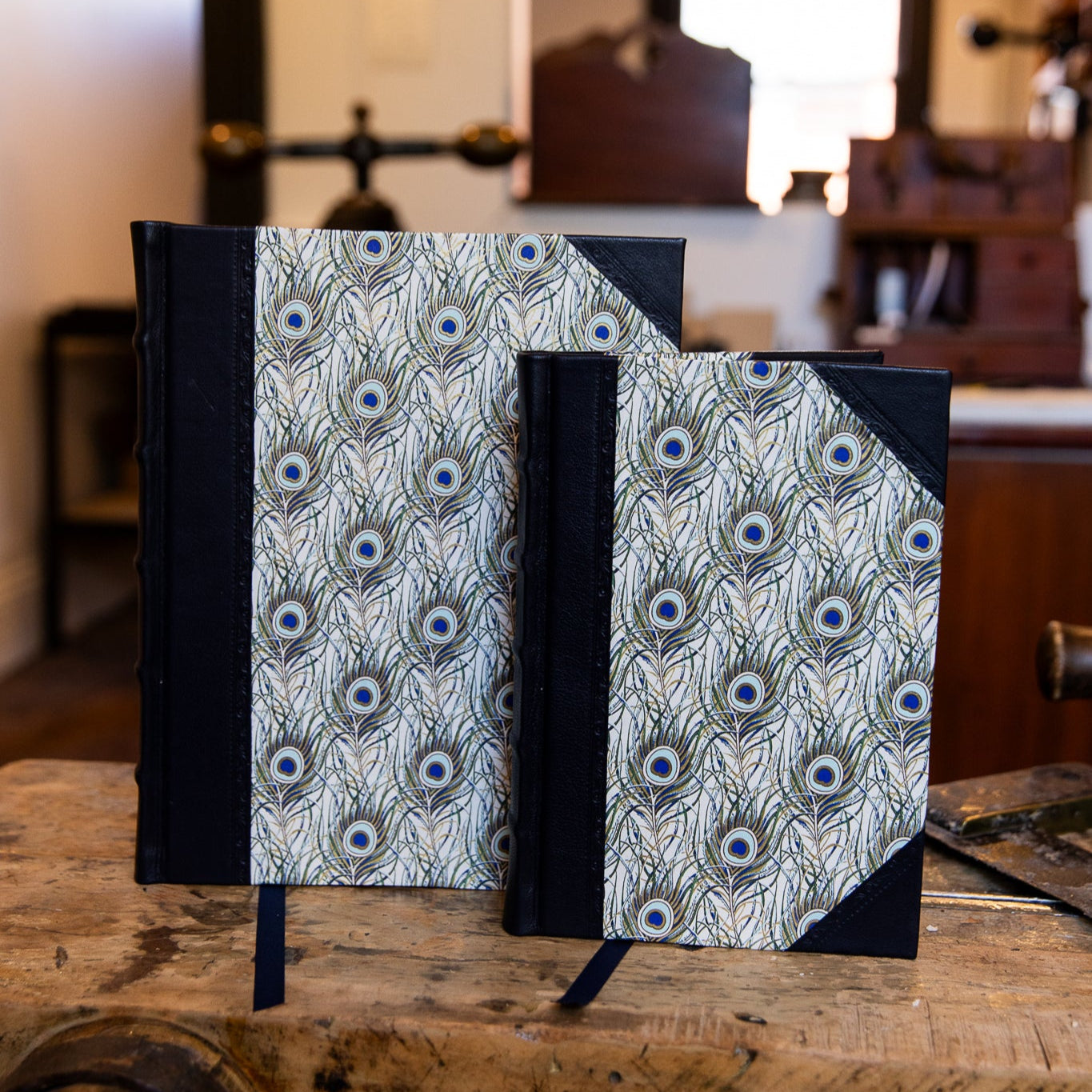Two SB Libris half leather journals with peacock feather design and navy leather spine, available in large and small sizes.