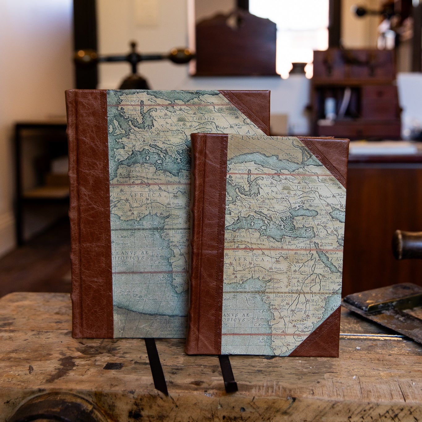 Two handcrafted SB Libris half leather journals with vintage world map covers and warm brown leather spines and corners.
