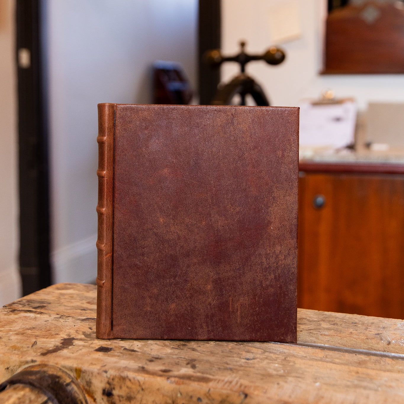 Brown leather-bound book on a wooden surface with a blurred indoor background